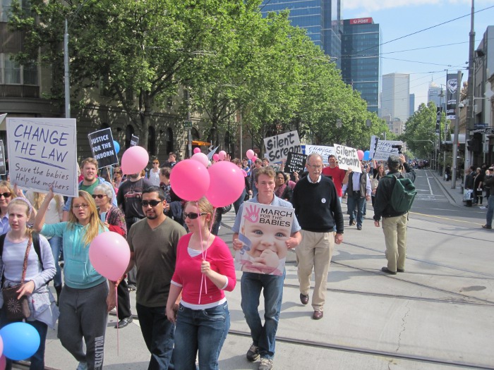 A diverse group of people, including young people and women, marching for the babies.